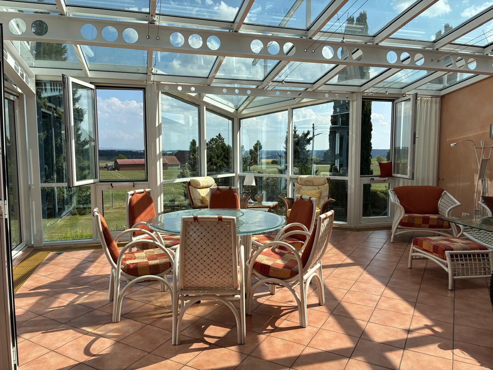 Sonniger Wintergarten mit Sitzgruppe und Blick über die Wiesen